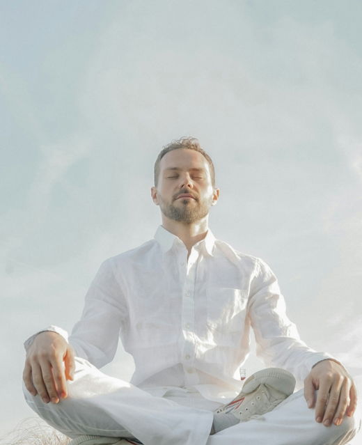 A man in a white shirt and tie sitting in a lotus position